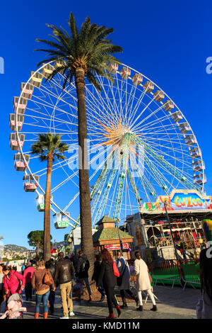 Place Masséna, Nizza, Frankreich, 5. Dezember 2017. Die Menschen genießen ein wunderschön sonnigen Tag mit blauem Himmel am schönen Weihnachtsmarkt. Die entspannte Atmosphäre des Marktes, mit Nahrung und Geschenk geht, Karussells, bunte Lichter und ein Riesenrad schön nimmt den Geist der Cote d'Azur festliche Jahreszeit. Stockfoto