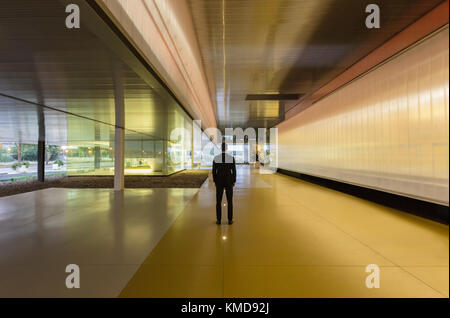 Ein Geschäftsmann steht in einem beleuchteten, modernen Büroflur in der Lobby Stockfoto