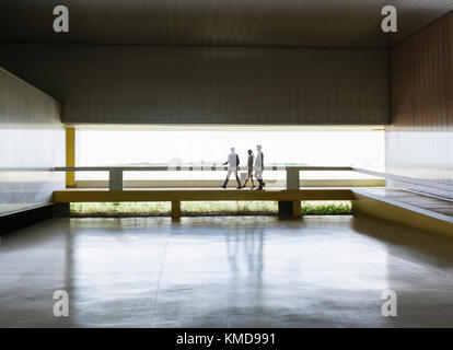 Geschäftsleute, die in der modernen Bürolobby über einen erhöhten Gehweg laufen Stockfoto