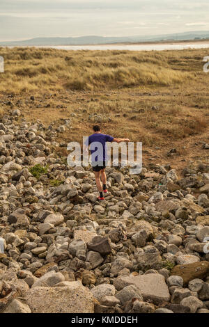 Ein Mann mittleren Alters jogg am Ufer entlang bei Paddys Hole, Redcar, England, Großbritannien Stockfoto