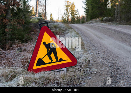 Verkehrsschild mit Warnung für die Arbeit, die von einer Schotterstraße Seite in einem Wald Stockfoto