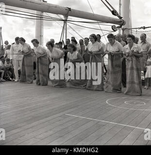 1950, historische, Schiff deck Spiele, weibliche Passagiere in postsäcken bis Zeile für ein Rennen auf dem Deck eines Union-Castle mailship Rubrik für Südafrika beobachtet von den anderen Passagieren und der Crew. Die union-castle Reederei mit Dampfer, waren eine beliebte Art und Weise zu diesem Zeitpunkt für eine Vielzahl von verschiedenen Menschen, Unternehmer, Staatsmänner, Reisende, die Einwanderer plus Fracht und Post ein Fernnetz für Übersee Ziel zu erreichen. Stockfoto