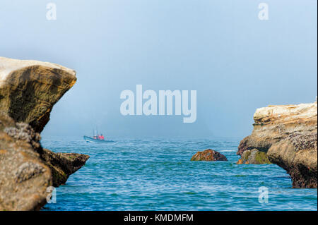 Pacific City, Oregon, USA - Juli 2, 2015: Haystack Rock durch Nebel gehüllt, als Ruderboot Boot seiner Landung am Strand navigiert am Cape Kiwanda in Pacific C Stockfoto