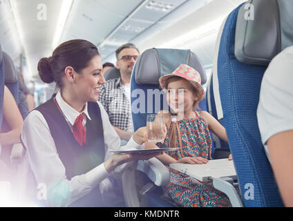 Weibliche Flugbegleiterin, die Mädchen im Flugzeug Wasser serviert Stockfoto