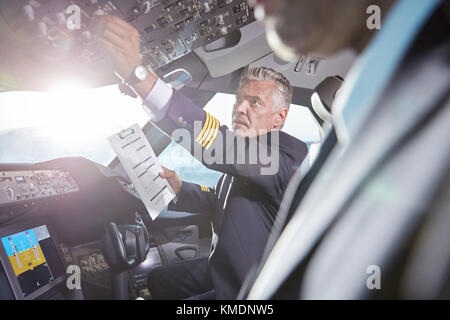 Männlicher Pilot mit Klemmbrett Vorbereitung, Anpassung Instrumente im Flugzeug-Cockpit Stockfoto