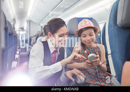 Flugbegleiter hilft Mädchen Passagier mit Fernbedienung im Flugzeug Stockfoto