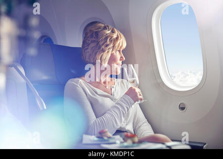 Reife Frau trinkt Champagner, Fenster in der ersten Klasse auf Flugmodus Stockfoto