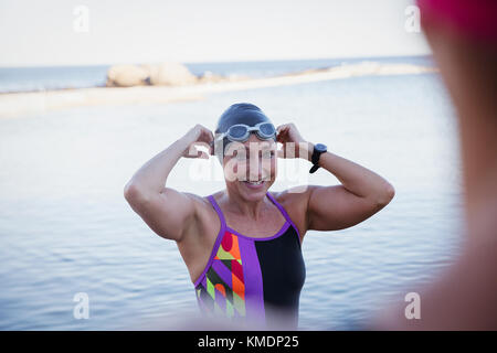 Lächelnde Schwimmerin mit offenem Wasser, die Badekappe und Schutzbrille anpasst Im Meer Stockfoto