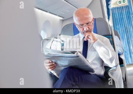 Geschäftsmann lesen Zeitung in Flugzeug Stockfoto