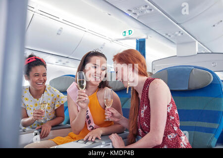 Junge Freundinnen lachen, trinken Champagner in der ersten Klasse im Flugzeug Stockfoto