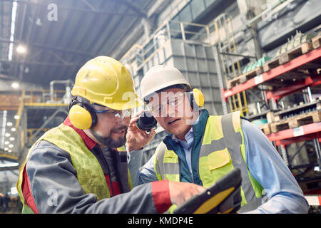 Stahlarbeiter tragen Gehörschutz mit digitalem Tablet in Stahlwerk Stockfoto