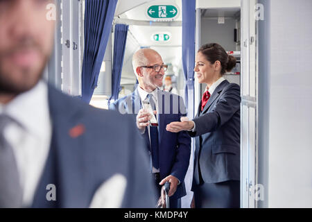 Flugbegleiter hilft Geschäftsmann mit digitaler Bordkarte im Flugzeug Stockfoto