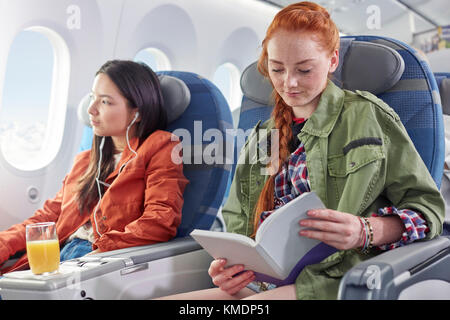 Junge Frau liest Buch im Flugzeug Stockfoto