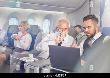 Geschäftsleute, die in der ersten Klasse im Flugzeug am Laptop arbeiten Stockfoto