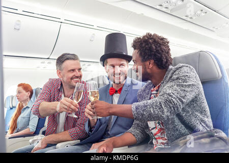 Junge männliche Freunde toasten Sektgläser in erster Klasse an Flugzeug Stockfoto