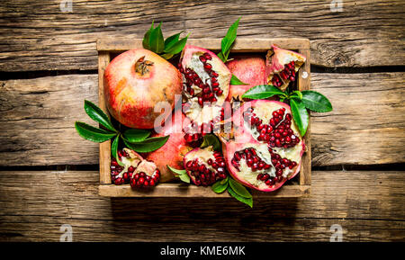 Frische granatäpfel in einer alten Box mit Blättern auf Holzuntergrund. top View Stockfoto