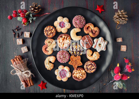 Weihnachtsplätzchen auf einer schwarzen Platte, Gewürze und Weihnachtsschmuck auf dunklem Hintergrund, Ansicht von oben, flach. Stockfoto