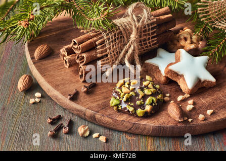 Weihnachten, close-up auf verschiedenen Cookies mit Nüssen, Zimtstangen, Klee und Weihnachtsbaum Zweige auf Holzbrett Stockfoto