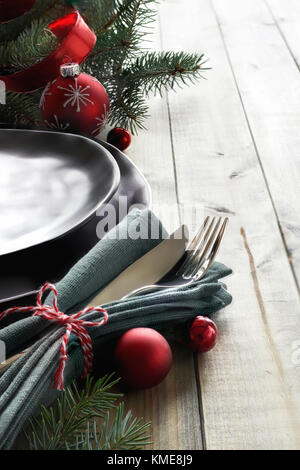 Weihnachtsmenü Konzept mit schwarzem Teller und Besteck mit Weihnachtsbaum Zweig und Bänder auf hölzernen Hintergrund gestaltet, in Türkis, Rot und Weiß. Stockfoto