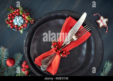 Weihnachtsmenü Konzept auf dunklem Hintergrund. Die schwarzen Platten und vintage Besteck mit Weihnachtsschmuck in Grün und Rot. Stockfoto