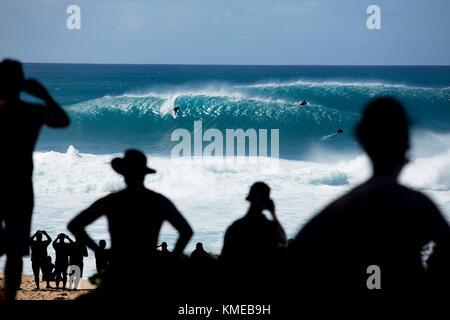 Silhouetten Zuschauer beobachten Surfer reiten riesige Wellen auf weltberühmten Banzai Pipeline, an der Nordküste von Oahu, Hawaii, USA Stockfoto