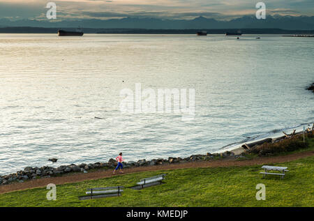 Ein Läufer Joggen entlang der Kante des Puget Sound in Seattle, WA an einem bewölkten Abend. Stockfoto