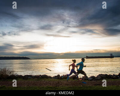 Zwei Läufer Silhouette gegen eine bunte Himmel entlang der Kante des Puget Sound in Seattle, WA. Stockfoto
