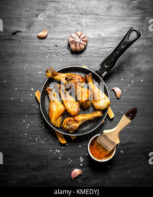 Gebratene Hähnchenkeulen mit Knoblauch und Soße. auf einem schwarzen Holz- Hintergrund. Stockfoto