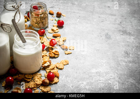 Fitness essen. Müsli mit Beeren und Milch in Flaschen auf dem Tisch aus Stein. Stockfoto