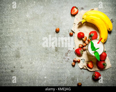 Milch Nachtisch mit Nüsse, Beeren und Bananen. Auf dem Tisch aus Stein. Stockfoto