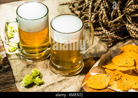 Zwei Bierkrüge mit Hopfen und Chips und Weizen Stockfoto