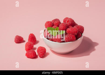 Schüssel mit frischen Himbeeren und Minzblättern auf rosa Hintergrund. Speicherplatz kopieren. Minimales Konzept. Hartes Licht. Stockfoto