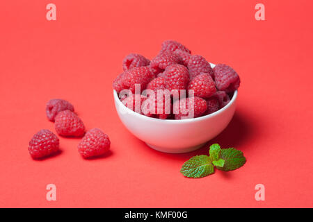 Schüssel mit frischen Himbeeren und Minzblättern auf rotem Hintergrund. Speicherplatz kopieren. Minimales Konzept. Hartes Licht. Stockfoto