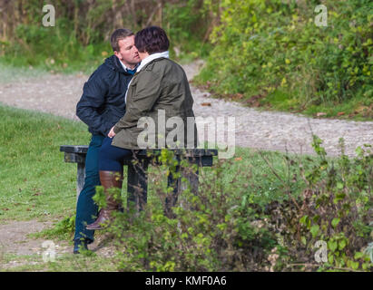 Paar draußen sitzen auf einer Bank, nahe kommen und zeigen öffentliche Zuneigung. Stockfoto