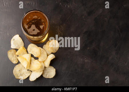 Nahaufnahme von altem Bier in einem langen Glas und von Kartoffelchips auf einem dunklen Stein mit Kopierfläche. Draufsicht. Stockfoto