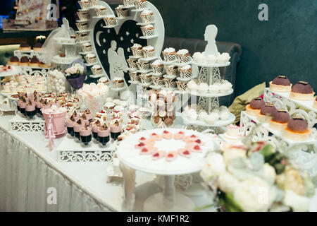 Schokoriegel mit verschiedene leckere Cupcakes, Macarons, Bonbons und andere Süßigkeiten für die Hochzeitsgesellschaft. rosa und weiss Komposition. Von der Seite. Stockfoto