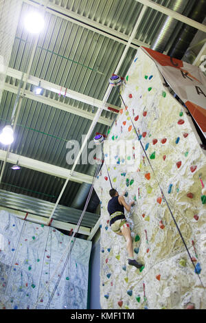 Junge athletische Kerl Kletterwand an künstlichen Wand. Stockfoto