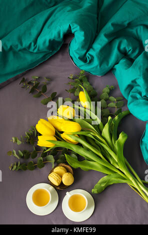 Gelbe Tulpen, Cookies und zwei Tassen Tee im Bett, Nahaufnahme Stockfoto