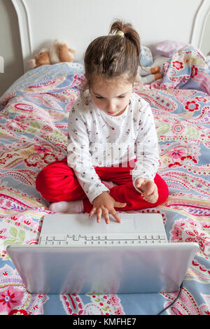 Kleines Mädchen im Bett sitzen und spielen Online-Spiele mit Laptop-computer Stockfoto