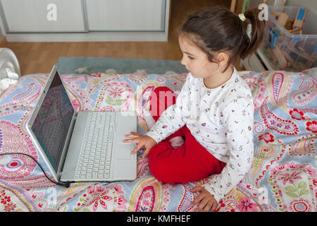 Kleines Mädchen im Bett sitzen und spielen online Spiele in Ihrem Schlafzimmer Stockfoto