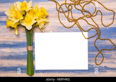 Einen Strauß Narzissen, ein weißes Blatt Papier und goldenen Perlen auf einer hölzernen Hintergrund. Frühling gelb Blumen. Papier mit Platz für Text. blue Peeling Stockfoto