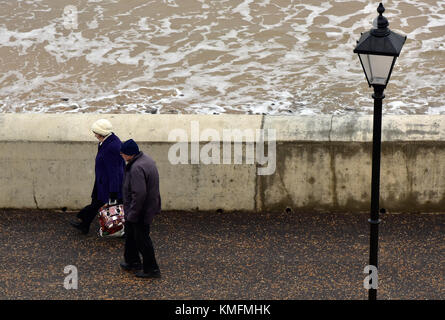 Eine ältere oder alternde Paar Spaziergang entlang der Küste bei Cromer in Norfolk an einem kalten Wintertag mit ihren wöchentlichen Einkauf in Tragetaschen. Stockfoto