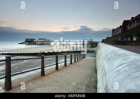 Ein Fußweg und Helling hinunter zum Strand und Meer bei Cromer in Norfolk mit der viktorianischen Pier und Rettungsboot Haus oder Bahnhof in der Ferne Stockfoto