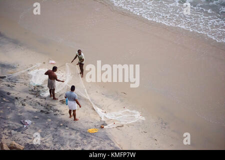 VARKALA, INDIEN - ca. Februar 2017: Drei Fischer entfalten und einem Fischernetz reinigen, nachdem sie an das Ufer zurück, am Varkala Strand in Indien. Stockfoto
