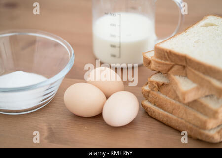 Alle Bestandteile von French Toast Rezept - Eier, Milch, Brot und Zucker auf hölzernen Hintergrund Stockfoto