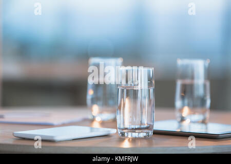 Wasser in der Brille neben digitalen Tabletten auf Tisch Stockfoto