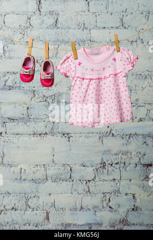 Baby rosa Kleid und rote Schuhe für das Mädchen, trocken auf einem Seil gegen eine weiße Wand. Stockfoto