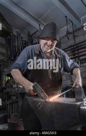 Der Schmied hagelt in der Werkstatt einen heißen Eisenstab auf den Amboss Stockfoto