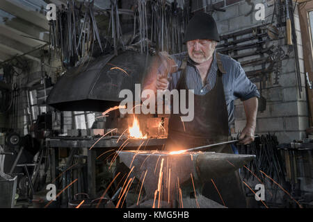 Der Schmied hagelt in der Werkstatt einen heißen Eisenstab auf den Amboss Stockfoto