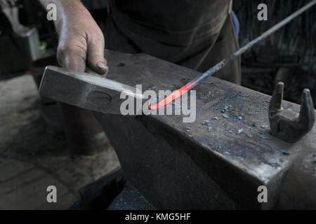 Der Schmied hagelt in der Werkstatt einen heißen Eisenstab auf den Amboss Stockfoto